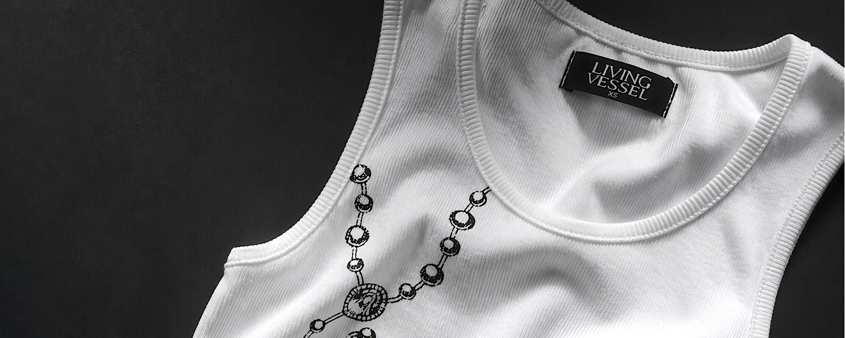 White tank top with a rosary and 'Living Vessel' label on a dark background